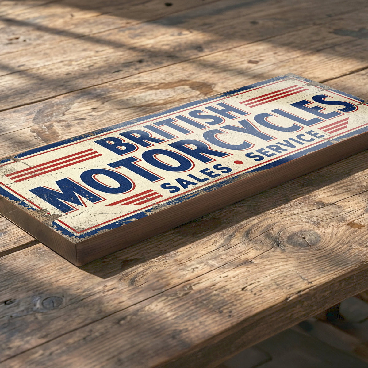 A rectangular vintage-style wooden sign reading “BRITISH MOTORCYCLES SALES SERVICE” in blue and red lettering on a distressed cream background, placed on a rustic wooden table.