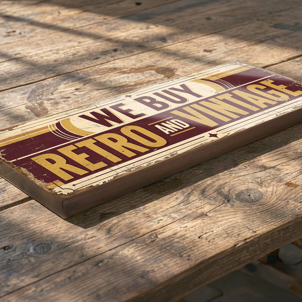 A rectangular wooden sign with a distressed retro design reading 'WE BUY RETRO AND VINTAGE' in yellow and cream lettering on a dark red and beige background, placed diagonally on a rustic wooden table.