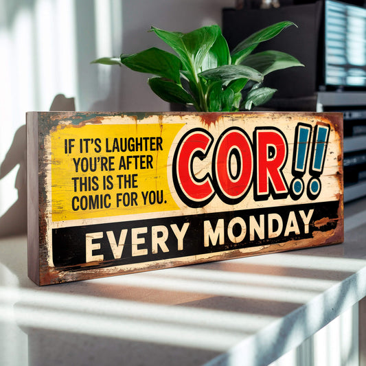 A rectangular vintage-style advertisement sign on 18mm MDF for the Cor!! comic. The design features red lettering, blue exclamation marks, and a yellow banner with heavy faux-rust and weathering effects.
