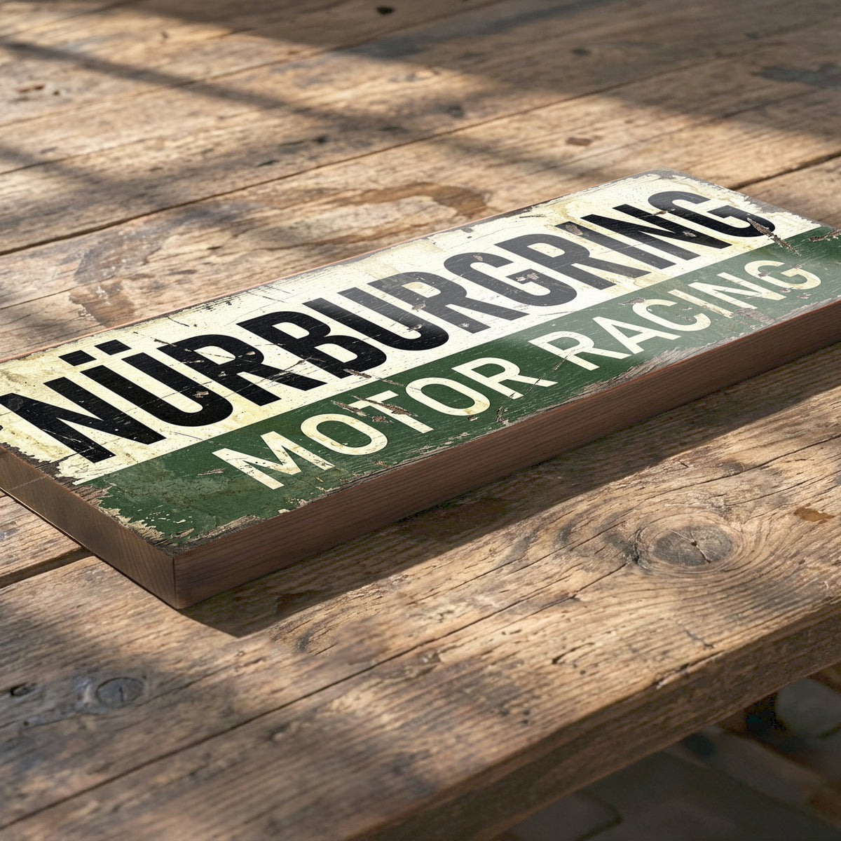 A rectangular wooden sign with distressed vintage lettering reading 'NÜRBURGRING MOTOR RACING,' placed diagonally on a rustic wooden table.