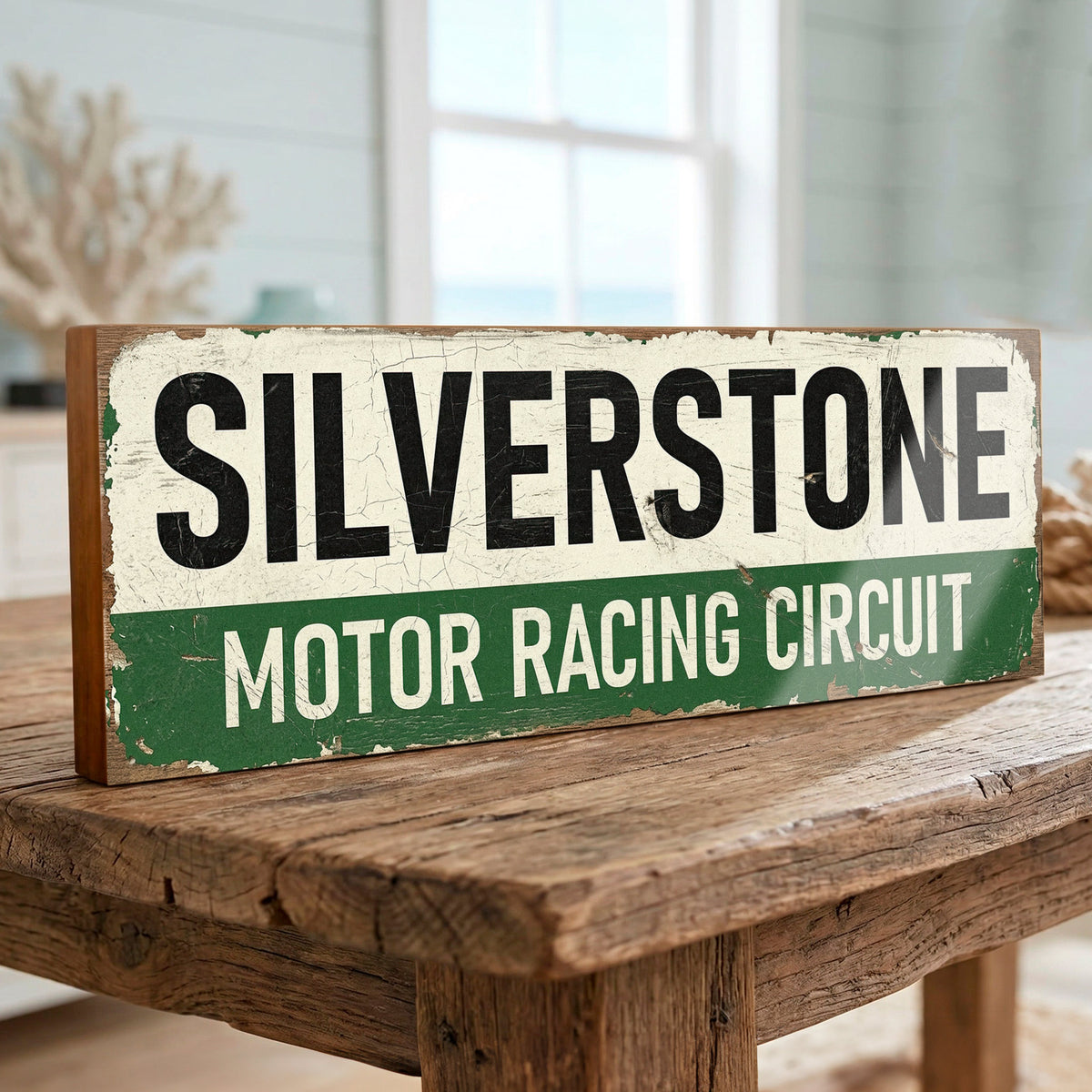 A rustic rectangular wooden sign reading “SILVERSTONE MOTOR RACING CIRCUIT” in black and white lettering on a distressed green and cream background, displayed on a rustic wooden table in a softly blurred indoor setting.