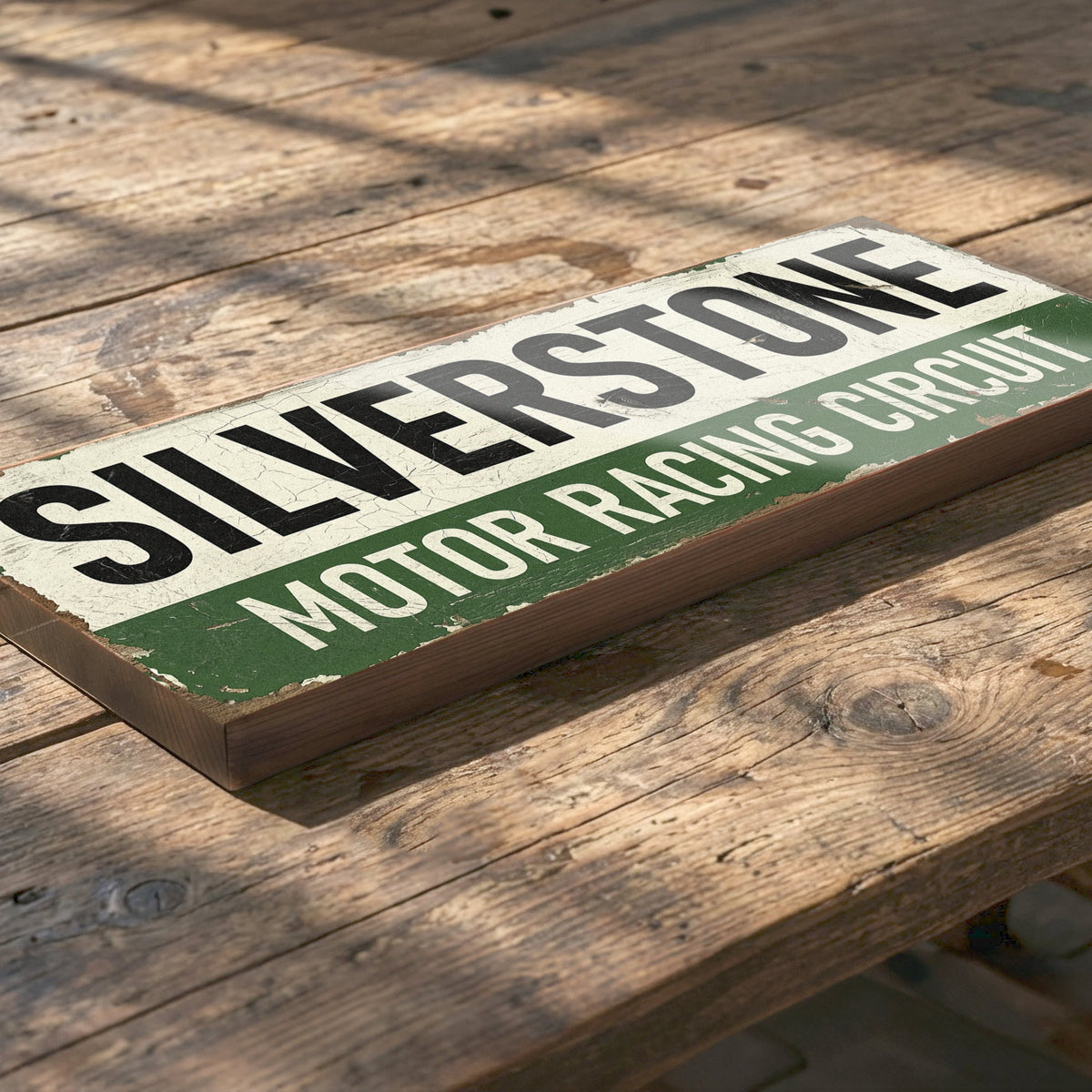 A rectangular wooden sign reading “SILVERSTONE MOTOR RACING CIRCUIT” in black and white lettering with a green stripe, placed on a rustic wooden table.